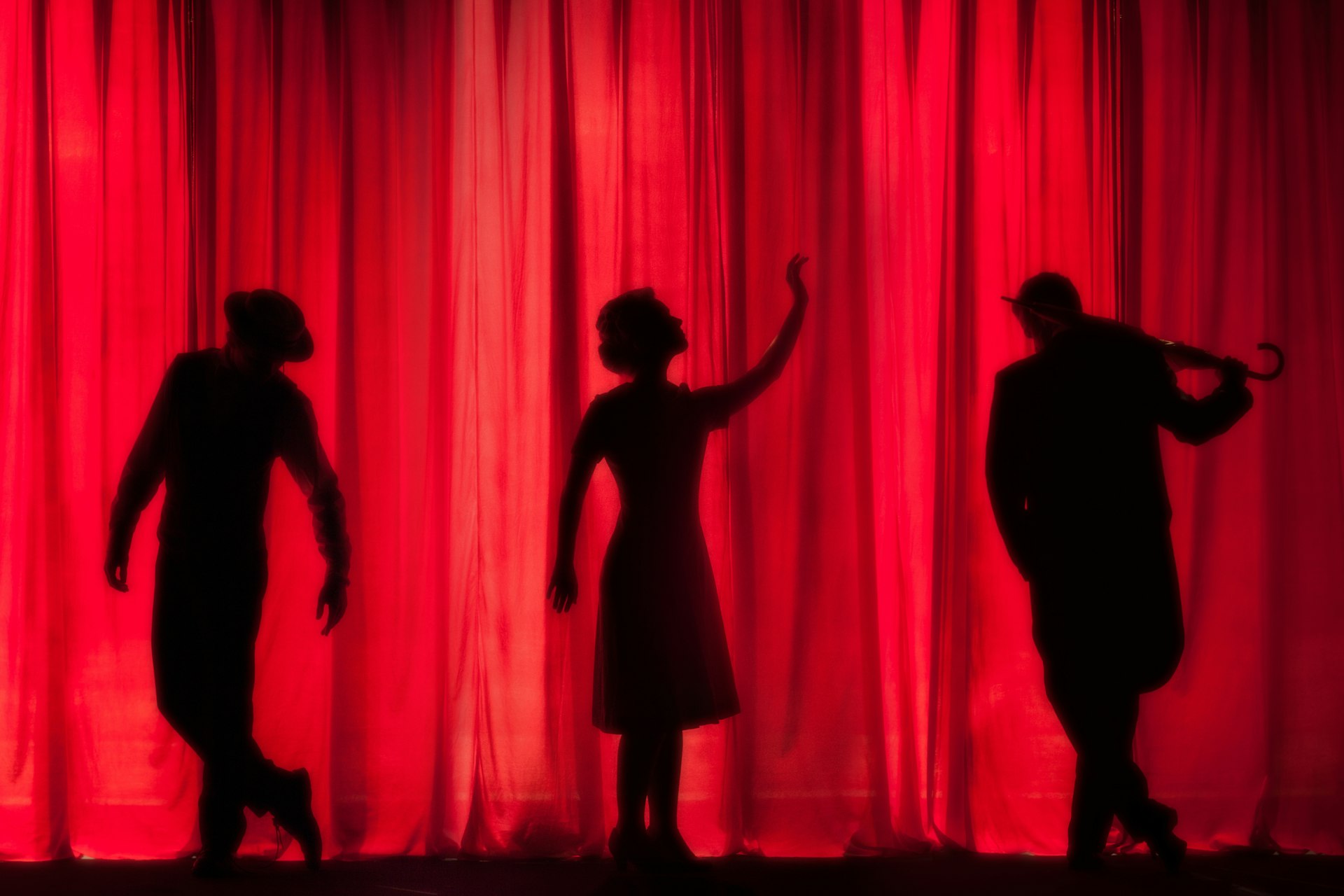 Performer silhouettes against a red curtain